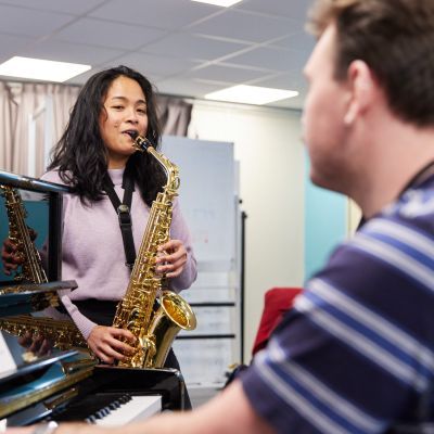 Music Therapy student in class playing piano and saxophone